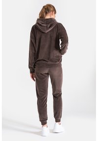Brązowy dres z polaru z kapturem, o luźnym kroju, z elastycznymi mankietami i dopasowanymi spodniami. Tkanina ma miękką, teksturowaną powierzchnię.