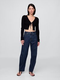 Schwarzes geripptes Crop-Top mit Front-Bindedetail, kombiniert mit hochgeschnittenen, lockeren, dunkelblauen Jeans und schwarzen Flip-Flops.