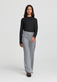 Top nero a maniche lunghe abbinato a pantaloni larghi grigi a coste; texture liscia, vestibilità comoda e scarpe nere piatte.