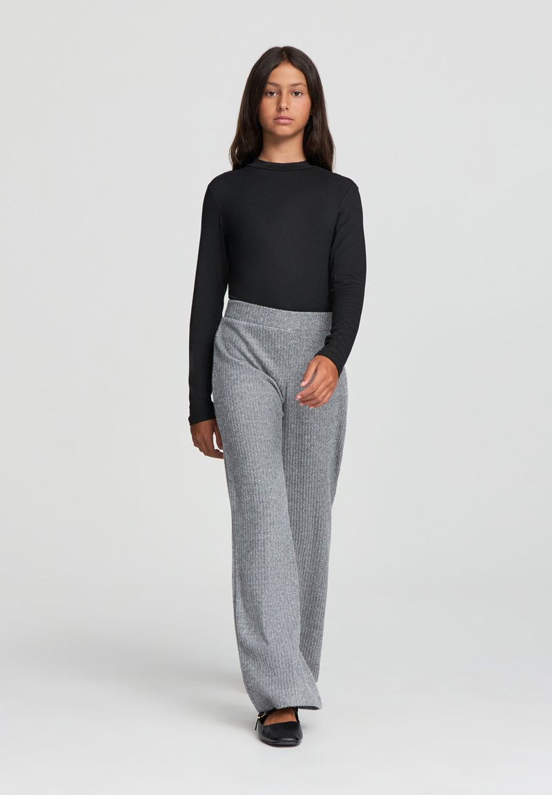 Top nero a maniche lunghe abbinato a pantaloni larghi grigi a coste; texture liscia, vestibilità comoda e scarpe nere piatte.