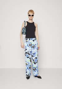 Top senza maniche nero, pantaloni blu con stampa floreale e dettagli neri e verdi, ballerine nere a punta e borsa teal.
