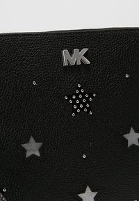 Sac à main en cuir noir avec une surface texturée, un logo argenté et des motifs d'étoiles décorés de strass de différentes tailles.