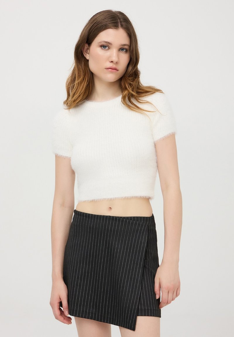 Maglione bianco, corto e peloso con maniche corte, abbinato a una gonna avvolgente nera a righe con un aspetto texturizzato e vita alta.