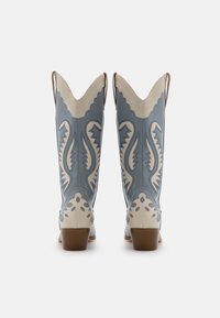 Světle modré kožené cowboy boty s bílým propracovaným šitím a vzory, špičaté špičky a krátké blokové podpatky.