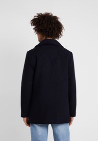 Cappotto in misto lana blu navy con colletto a revers, caratterizzato da una linea dritta e un design minimalista. Il tessuto presenta una texture liscia.