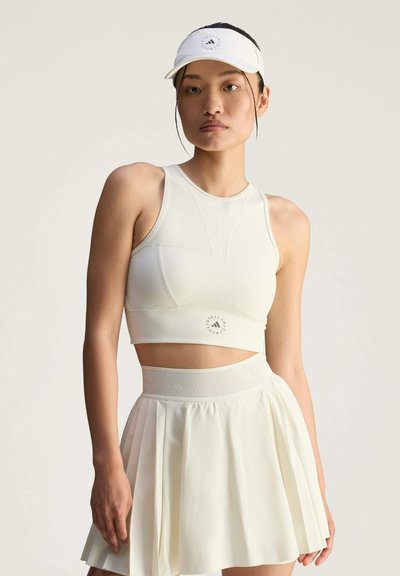 Top corto atlético blanco con un logo redondo y falda blanca plisada. Presenta un diseño ajustado y una cinturilla elástica, acompañado de una visera.