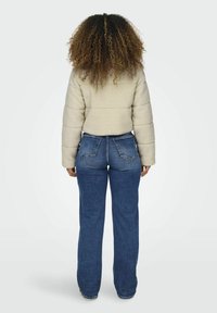 Beige pufferjack met een zachte stof en een gestructureerde afwerking, gecombineerd met blauwe denim flare jeans. Uitzicht van achteren.