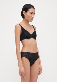 Svart blonde bralette og matchende truse sett med bølgete kanter, blomsterdesign og tynne stropper, med en jevn, strukturert overflate.