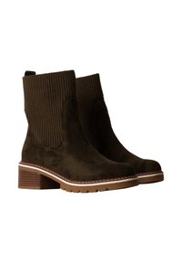 Botas de tobillo de ante marrón con tela ribeteada en la parte superior, tacón cuadrado y costuras blancas a lo largo de la suela. Acabado texturizado y punta redondeada.