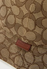 Brown fabric featuring an interlocking circle pattern, with textured accents. A stitched leather tag displays the brand name "COACH."