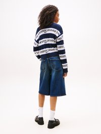 Námornícky a biely pruhovaný pletený sveter s logom "tommy jeans", v kombinácii s modrými riflovými šortkami po kolená a čiernymi platformovými topánkami.