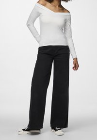 Vit off-shoulder långärmad topp i kombination med högmidjade vida svarta jeans och svarta sneakers med vita sulor.