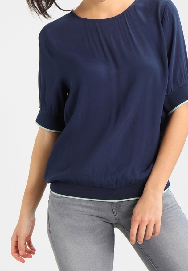 Námořnická modrá blůza s krátkými, volnými rukávy, zdobená kulatým výstřihem a elastickým lemem. Světle zelené akcenty po okrajích rukávů a dolním lemu.