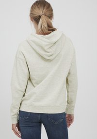Hellgrüner Hoodie mit einer weichen Textur, ausgestattet mit einer Zugkordel-Kapuze und gerippten Bündchen. Kombiniert mit dunkelblauen Jeans und minimalen Details.