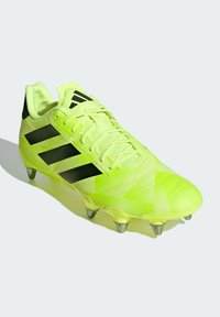 Crampon de football vert lime avec accents noirs, en matériau synthétique texturé, motif de design triangulaire et six crampons en métal sur la semelle.