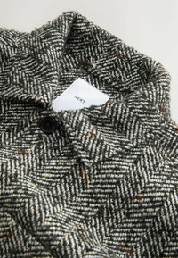 Sako s houndstooth vzorom s golierom, čiernym gombíkom a textúrovanou vlnou v odtieňoch sivej, bielej a hnedej.