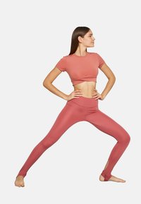 Top corto color rosa y leggings a juego, ambos hechos de un material suave y elástico, con detalles recortados en el tobillo para un estilo adicional.