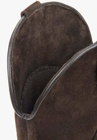 Wnętrze brązowego zamszowego botka do kostki, charakteryzujące się gładką teksturą i zaokrąglonym kształtem. Krawędzie wykończone czarną skórą dla kontrastu.