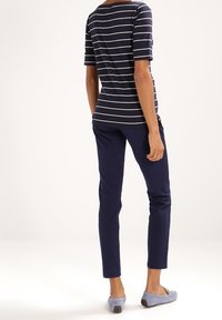 Marint randig t-shirt med kort ärm, i kombination med marint smala byxor och ljusblå platta skor, sedd bakifrån.