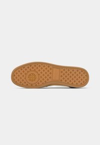 Semelle de chaussure en caoutchouc brun clair avec un motif de stries en diamant et un logo circulaire au centre, isolée sur fond blanc.