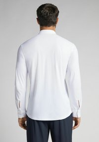 Witte blouse met lange mouwen en zijsplitten bij de manchetten, voorzien van een puntkraag en een soepele stof, gecombineerd met donkere broek.