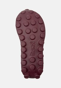 Burgundská guma podešev se zaoblenými vzory pro lepší trakci, texturovaným povrchem a embosovaným logem "CAMPER". Celkově hladký povrch.