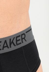 Svarta kalsonger för män med ett grått elastiskt midjeband som har ordet "SPEAKER" tryckt i svart. Tyget verkar mjukt med en diskret textur.