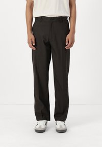 Brown, lightweight, tapered trousers with a flat front, side pockets, and a button closure, paired with white sneakers.