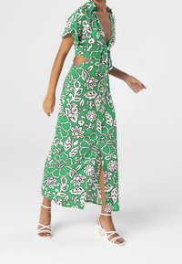 Groene bloemenmaxi-jurk met korte mouwen, uitsneden aan de zijkanten en een split aan de voorkant. Gemaakt van lichtgewicht stof met een levendig patroon.