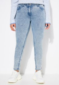 Vaqueros de mezclilla de color azul claro con un ajuste slim, con una cintura de altura media, cinco bolsillos y detalles cosidos a lo largo de las costuras, combinados con zapatillas blancas.