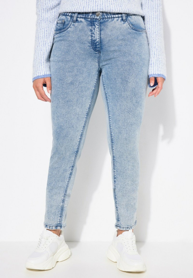 Vaqueros de mezclilla de color azul claro con un ajuste slim, con una cintura de altura media, cinco bolsillos y detalles cosidos a lo largo de las costuras, combinados con zapatillas blancas.