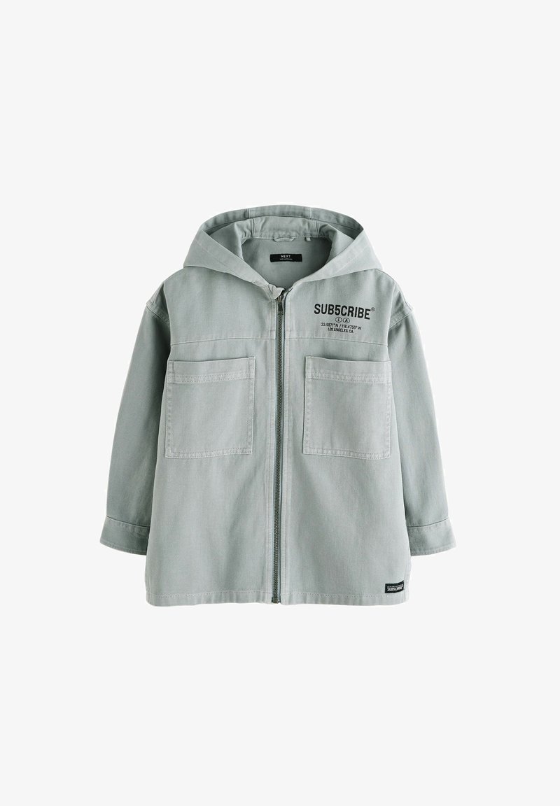 Heledad hallikas tõmblukkjakk, millel on kaks eesmist taskut ja rinnal tekst "SUBSCRIBE". Tekstuuriga kangas.