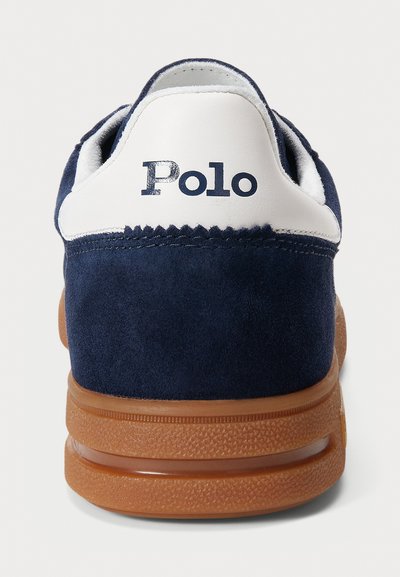 Tumesinine nokitsaga tennis, millel on valge nahkne konts ja tekstuuriga pruun kummitald, ning sinine "Polo" logo taga.