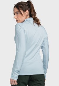 Hellblaues, langärmliges Sportoberteil mit strukturiertem Muster und hohem Kragen, das ein dezentes Markenlogo auf dem Ärmel trägt.