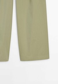 Moitié inférieure d'un pantalon beige à jambes droites avec des ourlets propres sur un fond blanc.
