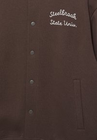 Brązowa bluza z kapturem z zatrzaskami, z haftowanym napisem „Steelbrook State Uniu.” po lewej stronie, z boczną kieszenią i gładką fakturą.