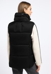 Czarna kamizelka puchowa z wysokim kołnierzem, detalami w postaci guzików i poziomymi pikowaniami, w połączeniu z kremowym swetrem z prążkowanej tkaniny.