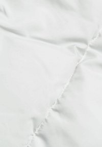 Gros plan d'un tissu blanc doux avec une couture visible et de légers plis sur une surface lisse.