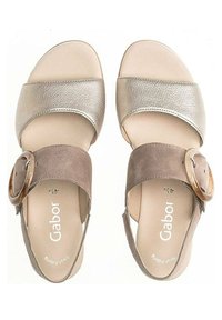 Two sandals with a beige leather strap, a taupe suede strap featuring a large round buckle, and a cushioned insole.