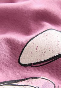 Rosa tyg med en strukturerad yta, som har ett grafiskt designelement i vitt och svart med glitterdetaljer och slitna inslag.