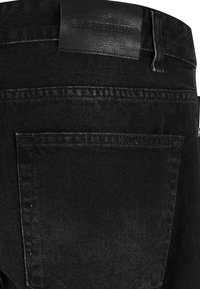 Mustmustest denim püksid, millel on nahkette tükkiga, millel on kiri "2Y PREMIUM." Disain sisaldab tagataskut ja horisontaalset õmblusdetaili.