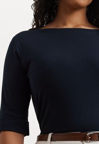 Top bleu marin cu gât în formă de barcă, mâneci trei sferturi și manșete răsucite, realizat dintr-un material neted, asortat cu o curea maro.