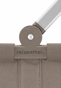 Cesta de almacenamiento Reisenthel con un patrón de espiga texturizado en beige, que cuenta con un asa metálica circular y un borde de tela gris plana.