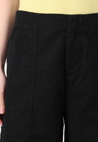 Pantalons en lin noirs avec une texture lisse, présentant une coupe droite, des poches latérales et un design de ceinture simple.