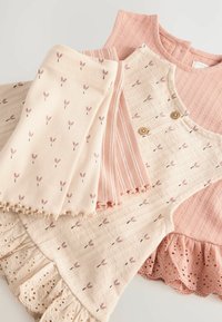 Twee pastelgekleurde kledingstukken gestapeld: een roze ribbel shirt, een crèmekleurige jurk met roze bloemenpatronen en kantafwerking, plus bijpassende leggings.