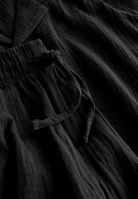 Czarny, teksturowany materiał o luźnym kroju z elastyczną talią i sznurkiem do wiązania. Zawiera styl przypominający kurtkę z kołnierzem.