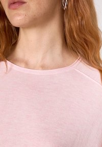 Růžový top z bavlněné směsi s kulatým výstřihem a raglánovými rukávy. Měkká textura s jemným melírováním. Žádné viditelné vzory ani ozdoby.