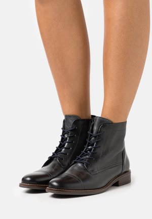 Bottes noires en cuir à la cheville avec un design nez de cap, comportant des lacets bleus, un col légèrement plus haut et une semelle plate marron.