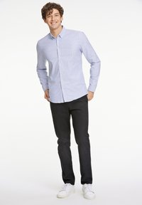 Ljust blå randig skjorta med knappar, kombinerad med mörka byxor och vita sneakers. Skjortan har krage och långa ärmar.