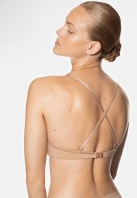 Beige bh met kruisbanden, een gladde textuur en een verstelbare band, met een minimalistisch ontwerp. Geen versieringen zichtbaar.